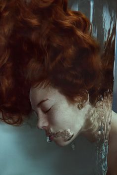 a woman with red hair is floating in the water and has her face partially submerged