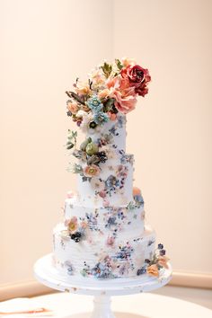 a wedding cake decorated with flowers on a white pedestal in front of a beige wall