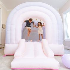 two children are jumping in an inflatable bounce house with balloons on the floor