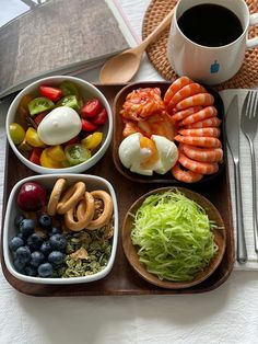 a wooden tray topped with different types of food next to a cup of coffee and utensils