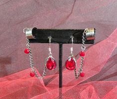 Make a bold statement with these Gothic Blood Red Pear Shaped Faceted Glass Earrings with Chained Ear Cuff. These earrings are the perfect embodiment of Gothic chic with a touch of horror aesthetic, making them a unique addition to your jewelry collection. Even better, they're not just for Halloween - every day is a good day to express your individuality and flair for the dramatic. The earrings are further accentuated with an ear cuff connected by a delicate chain. This chained ear cuff design adds an edgy twist to the classic drop earring, offering a blend of elegance and rebellion.  The ear cuff and chain design adds an edgy twist to the classic drop earring. It's a blend of elegance and rebellion, perfect for those who love to take fashion risks. *Products will be shipped within 1-3 bus Horror Aesthetic, Gothic Chic, Red Pear, Cuff Design, Delicate Chain, Blood Red, Drop Earring, Faceted Glass, Glass Earrings