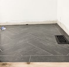 a bathroom floor with a grate in the middle and a trash can on the ground next to it