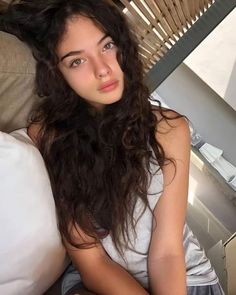 a young woman sitting on top of a bed next to a white pillow and wooden slatted wall