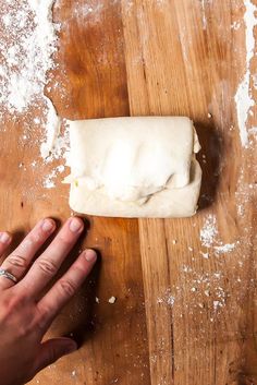 a person is kneading dough on top of a wooden table with their hand