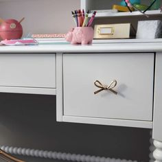 a white desk topped with lots of drawers and office supplies next to a pink pig figurine