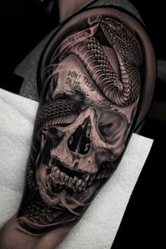 a man's arm with a skull and snake tattoo on it, in black and grey