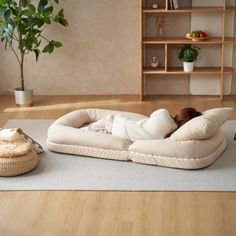 a woman laying on top of a dog bed next to a potted plant in a living room