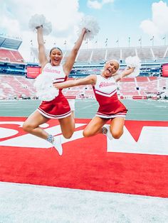 two cheerleaders jumping in the air at a football game