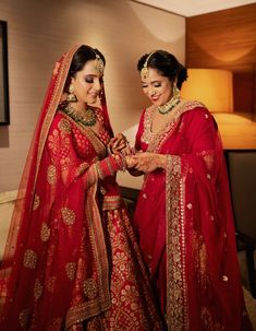 two women dressed in red and gold standing next to each other with their hands together