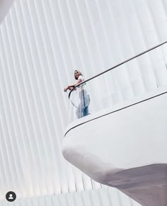 a man standing on top of a balcony next to a white wall with vertical blinds