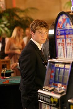 a young man in a suit standing next to a slot machine at a casino table