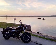 a motorcycle parked on the side of a road next to a body of water at sunset