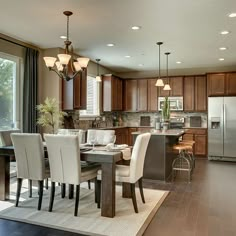 a dining room and kitchen area in a house with wood floors, large windows, and stainless steel appliances