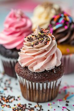 three cupcakes with pink frosting and sprinkles on a table