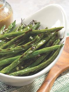 a white bowl filled with green beans next to a wooden spoon