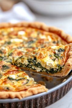 a quiche with spinach and cheese is being lifted from the pie pan by a spatula