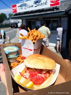 a person holding up a box with a sandwich and fries in front of a fast food restaurant