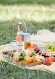 a bottle of wine sitting on top of a table next to fruit and crackers