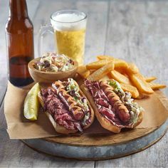 two hotdogs and fries on a wooden tray next to a bottle of beer