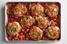 a pan filled with chicken, peas and lemons on top of a table next to a wooden spoon