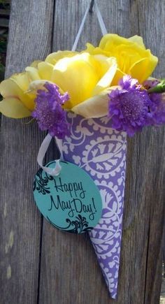 a purple and yellow flower arrangement hanging from a wooden fence with a happy mother's day tag