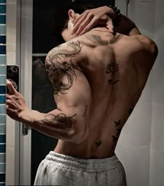 a man with tattoos on his back taking a selfie in front of a mirror