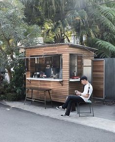 a man sitting on a chair in front of a small wooden building with an ice cream kiosk