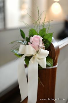 a pink rose and white ribbon tied to a wooden box with greenery in it