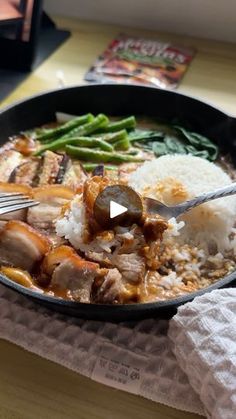 a pan filled with rice and meat on top of a wooden table next to a fork