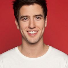 a young man smiling at the camera in front of a red background wearing a white t - shirt