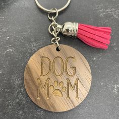 a wooden keychain that says dog mom with a pink tassel on it