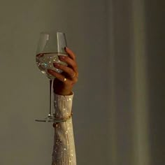 a woman's hand holding a wine glass in front of her face with glitter on it