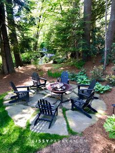 an outdoor seating area with chairs and fire pit in the middle of it, surrounded by trees