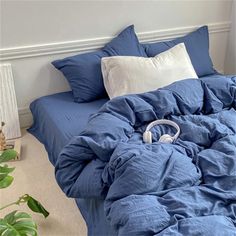 an unmade bed with headphones on it in a white room next to a potted plant