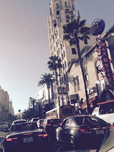 cars driving down the street in front of tall buildings with palm trees on both sides