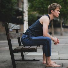 a young man sitting on a bench in the middle of a city street with his feet crossed