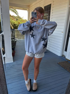 a woman taking a selfie in front of a house with her cell phone and shoes on