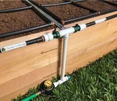 two garden hoses are attached to the side of a wooden planter box with soil in it