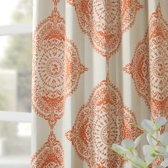 an orange and white curtain hanging on a window sill next to a vase with flowers in it