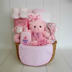 a pink teddy bear sitting in a basket filled with baby items