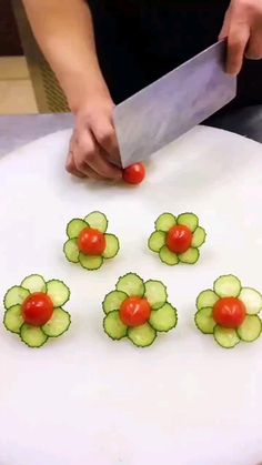 a person cutting cucumbers with a knife on top of a white plate topped with tomatoes and cucumber slices