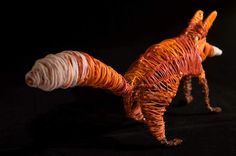 an orange and white cat made out of yarn on a black surface with a light behind it