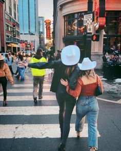 two people walking across a street in the middle of a crosswalk, with one person wearing a cowboy hat on his head