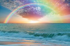 a rainbow in the sky over an ocean with waves crashing on the shore and clouds above