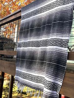 a black and white blanket hanging on a wooden deck next to a tree with orange leaves