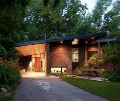 a modern house in the woods with lights shining on it's windows and doors