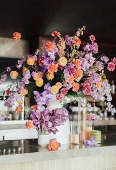 a vase filled with lots of flowers on top of a counter next to candles and bottles