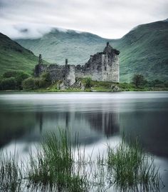 a castle sitting on top of a lush green hillside next to a lake and mountains