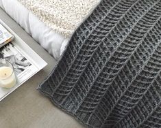 a knitted blanket sitting on top of a bed next to a book and candle