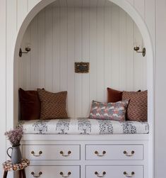 a white bench with pillows on top of it and some drawers in front of it